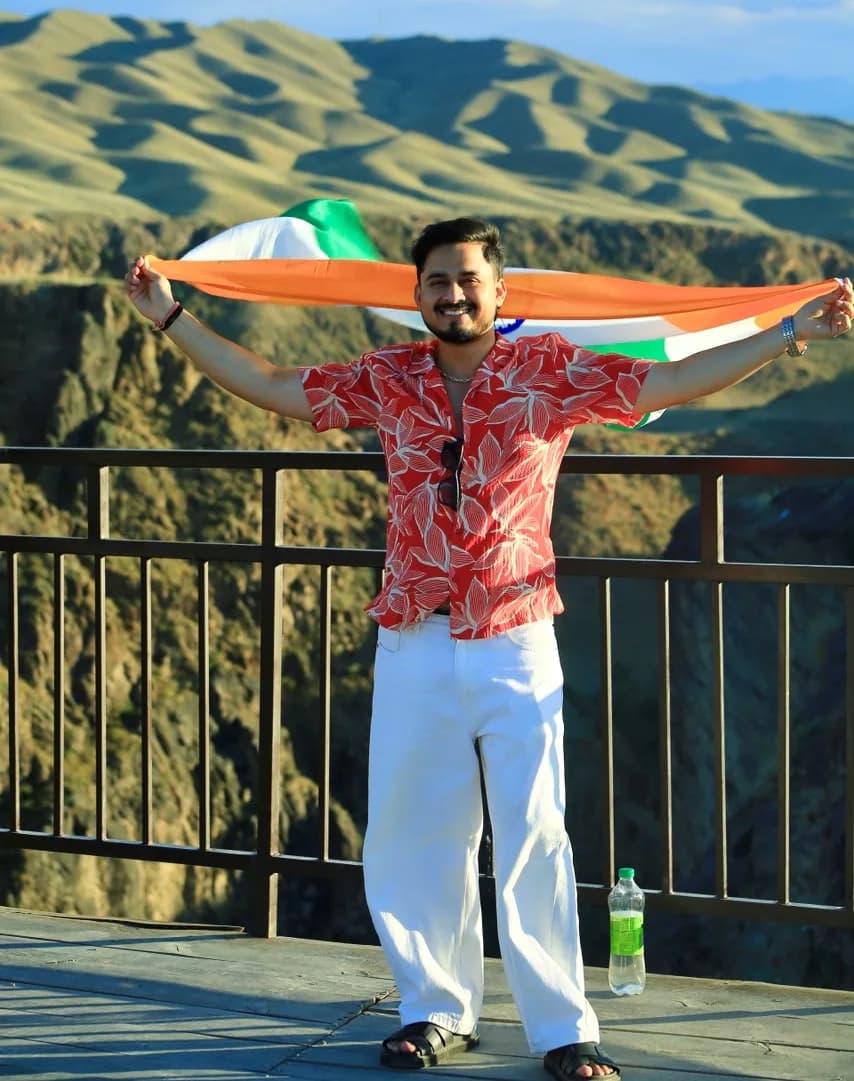 Lucky Rohilla holding the Indian tricolour open above his shoulders on a mountain viewpoint — founder of Lucky Bharat.
